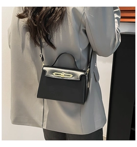 Side view of matte black leather handbag with gold bar lock on model in formal attire