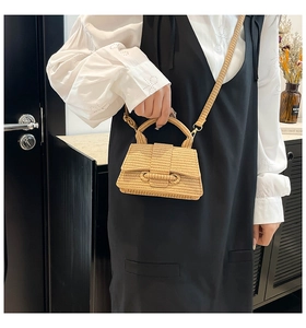 Detail of a beige woven straw bag featuring a trapezoidal shape and adjustable shoulder strap