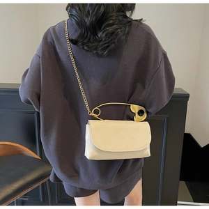 Détail d'un sac en cuir blanc crème avec une grande épingle de sûreté dorée et chaîne