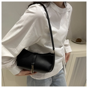 Detail shot of a black leather shoulder bag with a sleek golden metal clasp on a model