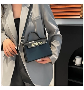 Detail of elegant black trapezoid handbag with gold metal bar lock and leather strap