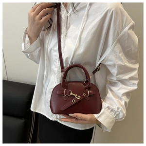 Detail of burgundy shell-shaped crossbody bag with gold metal hook and leather strap