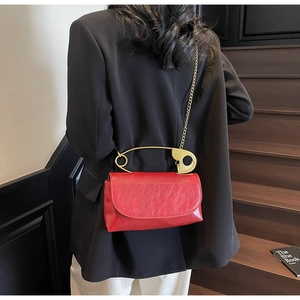 Detail of red square bag with a large gold safety pin handle and metal chain strap
