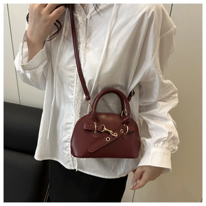 Detail of burgundy shell-shaped crossbody bag with adjustable strap and gold hardware