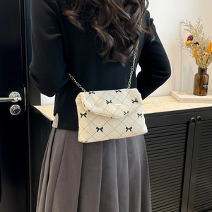 Cream corduroy shoulder bag with black bow print and gold chain strap on model