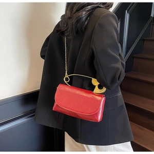 Detail of red leather crossbody bag with creative gold safety pin handle and chain