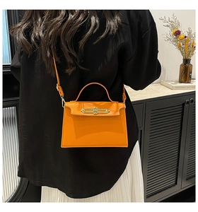 Orange leather trapezoid handbag with gold buckle shown in a lifestyle home setting