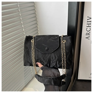 Détail de la texture plissée noire et de la bandoulière en chaîne dorée du sac à main