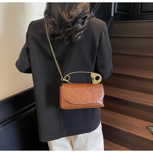 Back view of model wearing a vintage brown faux leather crossbody bag with oversized safety pin handle
