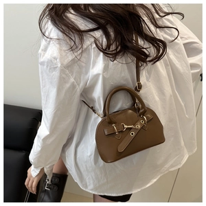 Brown mini shell bag with unique gold buckle and leather strap shown on a model