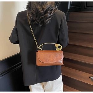 Détail du sac en cuir marron avec poignée épingle de nourrice dorée et bandoulière chaîne