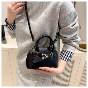 Detail of black mini shell bag featuring matte leather texture and gold metal hardware hooks