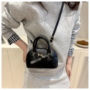 Detail of a black mini shell bag featuring matte leather and a gold buckle on the strap