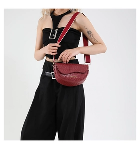 Detail of dark red saddle bag featuring woven texture and a wide striped strap
