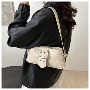Detail of cream croc-embossed baguette bag with silver buckle on a black leather jacket