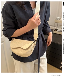 Detail of a beige crocodile pattern saddle bag with wide strap on a model