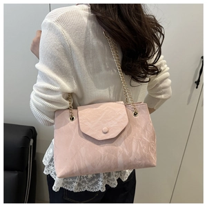 Détail d'un sac rose clair avec texture pierre et chaîne dorée porté par un modèle