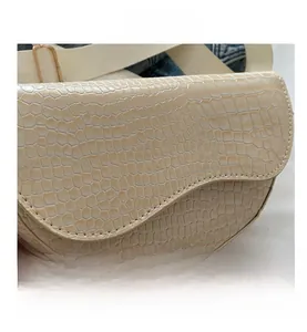 Close-up of cream crocodile pattern saddle bag with wide fabric shoulder strap