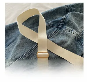 Detail of adjustable beige nylon strap with gold metal buckle on denim jacket