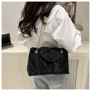 Détail du sac à bandoulière noir texture froissée avec chaîne dorée porté par mannequin