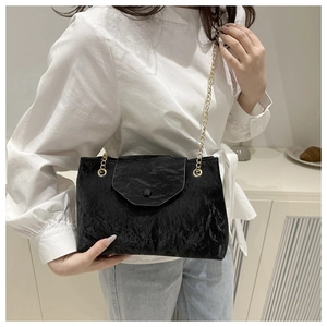 Close-up of black pleated crossbody bag with golden chain strap on model for styling