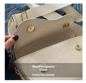 Detail showing the magnetic metal buckle on a beige crocodile pattern saddle bag