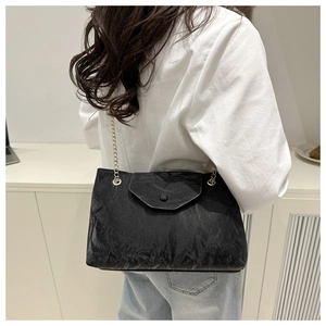 Détail d'un sac cabas noir plissé avec bandoulière chaîne dorée porté par un mannequin