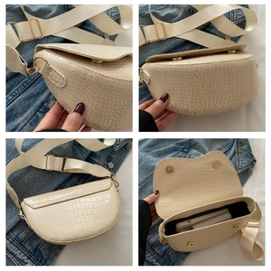 Detail view of cream crocodile embossed saddle bag with gold buckle and wide strap