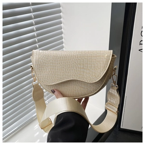Detail of beige crocodile embossed saddle bag with wide nylon strap and gold hardware