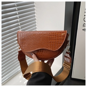 Detail of caramel brown croc-embossed saddle bag with wide canvas strap and gold buckle