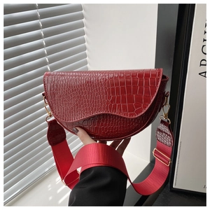 Close-up of red crocodile embossed saddle bag with wide strap and gold hardware