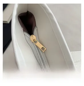 Détail de la fermeture éclair dorée et du cuir blanc à texture litchi du sac