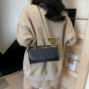 Minimalist black pleated shoulder bag with unique gold pin handle and chain strap on model