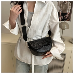Detail of black crocodile texture saddle bag with wide fabric strap and gold hardware