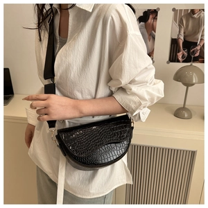 Close-up of black croco-embossed saddle bag with wide fabric strap and asymmetric flap