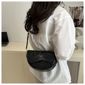 Detail of black crocodile embossed saddle bag with gold metal hardware on model