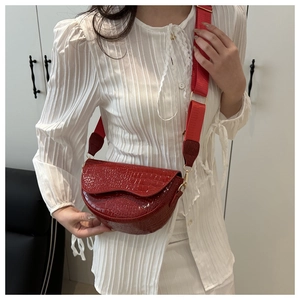 Close-up of red crocodile embossed saddle bag with stylish wide fabric shoulder strap