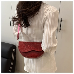 Detailed side view of a red crocodile pattern saddle bag with fabric shoulder strap