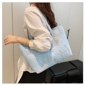 Detail of light blue tote bag with embossed textures and colorful wavy stitching