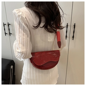 Detailed close-up of dark red embossed crocodile leather saddle bag with wide strap