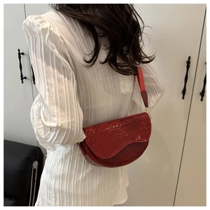 Detail of red crocodile texture saddle bag with gold hardware and wide shoulder strap