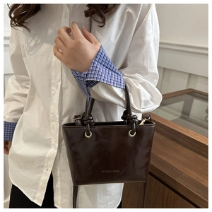 Dettaglio borsa a secchiello in pelle marrone scuro con logo dorato e fibbia in metallo