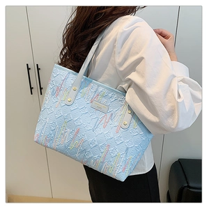Détail du sac cabas bleu clair avec broderie ondulée et plaque de marque en métal