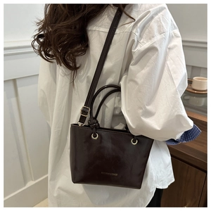 Dettaglio della borsa tote marrone scuro con logo dorato e manico con nodo chic