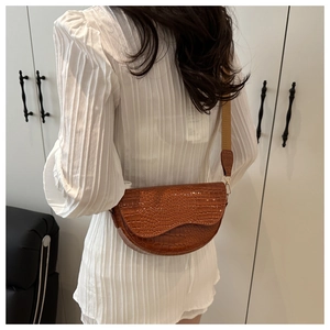 Detail of brown crocodile embossed saddle bag with wide khaki fabric shoulder strap