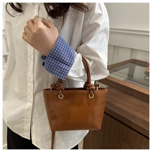 Dettaglio della borsa tote in pelle marrone caramello con manico annodato e anelli dorati