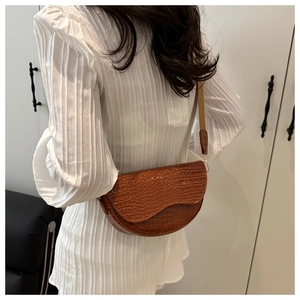 Detail shot of brown crocodile embossed leather saddle bag with slim shoulder strap