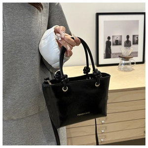Dettaglio della borsa nera lucida con scritta Fashion & Bags e hardware in metallo dorato