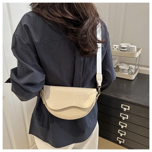 Detail of a creamy white crocodile pattern saddle bag with unique wavy edge flap design