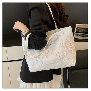 Detail of white tote bag featuring textured embossing and colorful wave embroidery detail